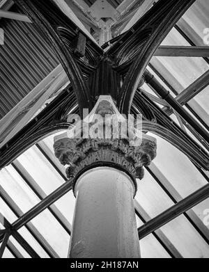 Blick nach oben auf eine historische korinthische Säule aus dem 19. Jahrhundert, die einen Baldachin stützt. Ein Oberlicht wirft Licht auf ein kompliziertes Eisenwerk. Stockfoto