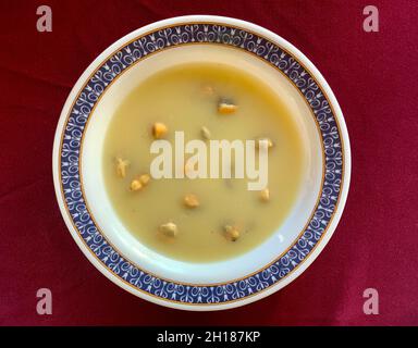 Haute Cuisine, perfekt präsentierte Muschelsuppe auf weißem Teller mit roter Dekoration Stockfoto