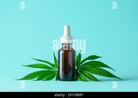 CBD-Öl oder Tinktur in brauner Glasflasche mit Cannabisblättern auf minimalistischem Aqua-Hintergrund mit Kopierraum Stockfoto