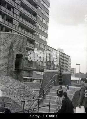 Sechziger Jahre, historisch, Kinder draußen neben einem Beton- und Backsteinspielplatz, in einem großen wohngebiet des rates, Churchill Gardens in Pimlico, im Inneren von London, England, Großbritannien. Zwischen 1948 und 1962 erbaut, um viktorianische Terrassen zu ersetzen, die im Blitz des 2. Weltkrieges beschädigt wurden, war dies ein riesiges Anwesen moderner sozialer Wohnhäuser mit 32 Turmblöcken, die 1,600 Häuser bieten. Stockfoto