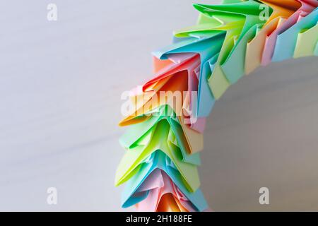 Origami-Ringfragment, abstrakte parametrische Struktur aus bunten Papierblättern, liegt auf einem weißen Holzschreibtisch, Draufsicht Stockfoto