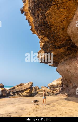 Eine vertikale Aufnahme einer jungen Frau, die mit dem Hund am Meer in Playa de Garcey, Westküste von Fuerteventura, Kanarische Inseln, Spanien, läuft Stockfoto