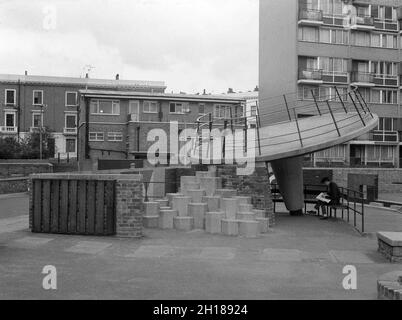 Die 60er Jahre, historisch, ein betonierter Spielplatz außerhalb eines großen wohngebiets des rates, Churchill Gardens in Pimlico, im Inneren Londons, England, Großbritannien. Zwischen 1948 und 1962 erbaut, um viktorianische Terrassen zu ersetzen, die im Blitz des 2. Weltkrieges beschädigt wurden, war dies ein riesiges Anwesen an sozialem Wohnraum mit 32 Turmblöcken, die 1,600 Häuser bereithalten. Auf dem Bild sieht man einen jungen Mann, der auf einer Bank unter einer betonierten Spielplatzuntertasse mit Geländer sitzt, mit sechseckigen Stufen nach oben. Stockfoto