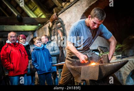 17. Oktober 2021, Sachsen, Olbernhau: Der handwerkliche Schmied Thore Krauter (r) zeigt seinen Besuchern sein Handwerk während einer Schauschmiede im Kupferhammer in der Saigerhütte. Am 22. Tag des traditionellen Handwerks im Erzgebirge öffnen zahlreiche Handwerksbetriebe aus verschiedenen Gewerken ihre Türen. Foto: Kristin Schmidt/dpa-Zentralbild/ZB Stockfoto