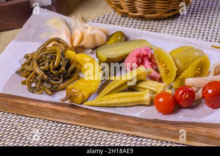 Verschiedene Arten von eingelegtem Gemüse auf einem weißen Teller. Eingelegte Gurken, Tomatenkirschen, Gemüse, Pilze und Knoblauch mit Zwiebeln und Salat auf der t Stockfoto