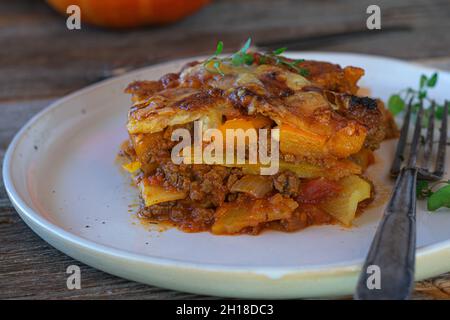 Glutenfreie Auflaufform mit Hackfleisch, Kartoffeln und hokkaido-Kürbis. Garniert mit geschmolzenem Mozzarella-Käse und serviert auf dem Teller mit Gabel Stockfoto