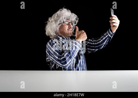 Lächelnder Mann, der am Schreibtisch sitzt und einen Videochat auf dem Smartphone auf schwarzem Hintergrund unterhält Stockfoto