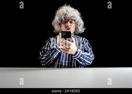 Mann, der am Schreibtisch sitzt und einen Kuss bläst und einen Videochat mit einem Smartphone auf schwarzem Hintergrund führt Stockfoto