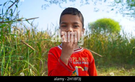 15. Oktober 2021 Reengus, Rajasthan, Indien. Porträt des kleinen Jungen zeigt Sieg Hand Zeichen auf grünem Feld Hintergrund Stockfoto