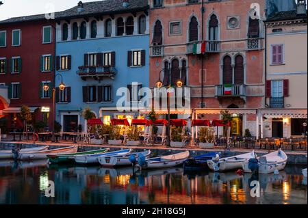 An der Meeresmauer wurden Boote befestigt, und in der Abenddämmerung romantische Cafés am Wasser. Desenzano del Garda, Lago di Garda, Lombardia, Italien. Stockfoto