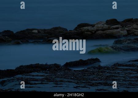 LANGZEITBELICHTUNG BEI NACHT, BILD DES DRAMATISCHEN HIMMELS UND DER WELLENLANDSCHAFT MIT FELSEN IM LANDSCHAFTSHINTERGRUND. Stockfoto
