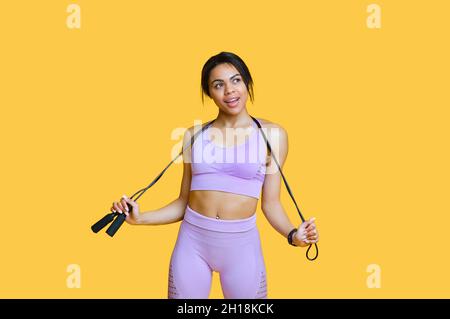 Sport für jeden Körper. Fit schwarze Frau hält Springseil, posiert in Sportkleidung über gelben Hintergrund, freien Raum Stockfoto