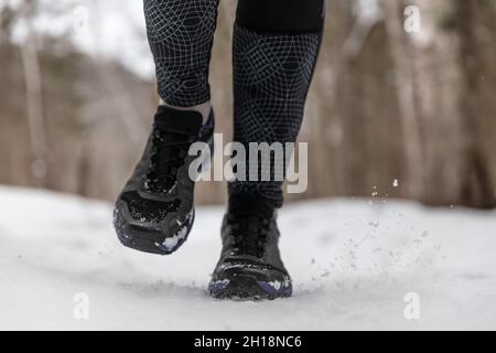 Winterlaufschuhe Frau trainiert im Freien Kardio beim Joggen auf weißem Schnee bei kaltem Wetter. Nahaufnahme der Füße mit Fitnessschuhen Stockfoto