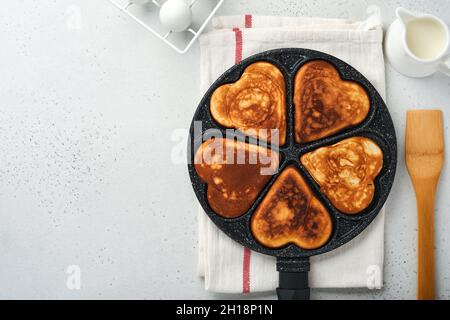 Pfannkuchen in Form Herzen mit Schokoladensauce in grauer Keramikplatte, Tasse Kaffee auf grauem Betongrund. Tischeinstellung für Ihren Favoriten Valent Stockfoto