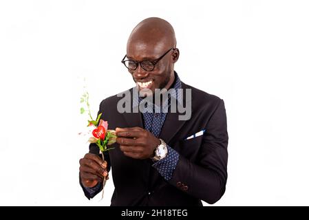 Schöner lächelnder junger Mann mit schwarzer Jacke und Brille, der einen Blumenstrauß hält und berührt; mach dich bereit für einen Termin mit seiner Freundin Stockfoto