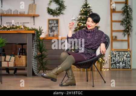 Kurze Haare Brünette Frau mit einem Glas Champagner sitzt auf einem Stuhl Weihnachten feiern. Stockfoto