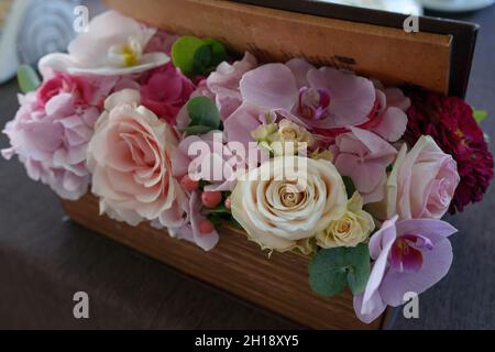 Rechteckige Holzkiste mit einem Blumengesteck in Pastelltönen mit Rosen, Orchideen und Beeren, floralem Tischdekor und organischem Dekor Stockfoto