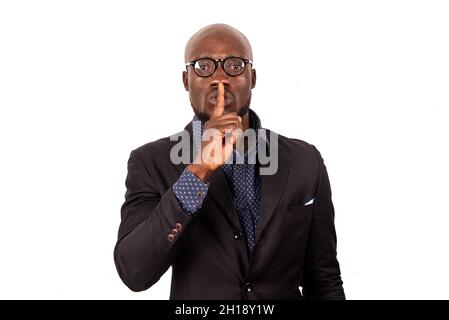 Junger Geschäftsmann im Anzug, der auf weißem Hintergrund mit dem Finger auf den Lippen steht und Zeichen der Stille zeigt. Stockfoto