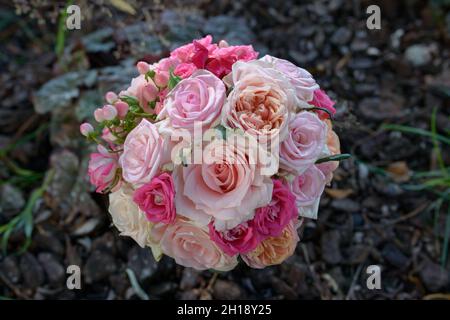 Blick von oben auf einen eleganten runden Brautstrauß mit Rosen in verschiedenen Rosa-Farbtönen, Hypericum-Beeren und seidig pastellfarbenen Pfirsich-Pfingstrosen Stockfoto