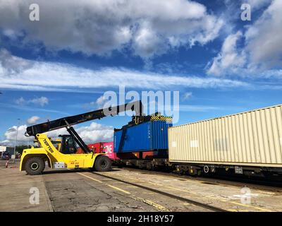 Eine Maschine mit Schwerlastkran, die einen Transportcontainer an einem kommerziellen Terminal oder Dock auf einen Güterzug verlädt Stockfoto