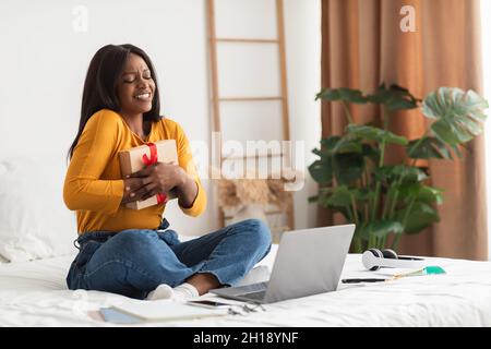 Afrikanische Frau Umarmt Geschenkbox Während Videoanruf Zu Hause Stockfoto