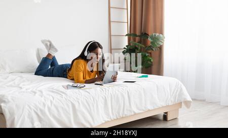 Schwarze Frau, Die Ein Tablet Benutzt, Kopfhörer Trägt Lernen Im Schlafzimmer, Panorama Stockfoto