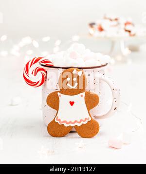Fröhliche Lebkuchenfrau Weihnachtsplätzchen vor einem Becher heißer Schokolade. Helle Urlaubsszene mit Pink, Rot und Weiß. Stockfoto