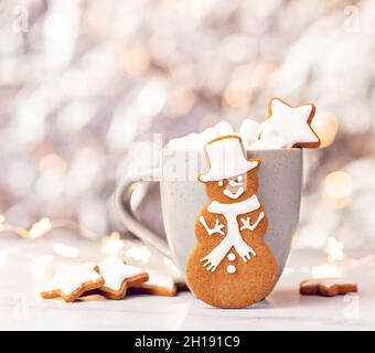 Niedlicher Lebkuchen Schneemann Cookie vor einer Tasse heiße Schokolade mit Marshallows. Hübscher Bokeh-Hintergrund. Stockfoto