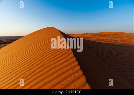Fußabdrücke entlang des Rückens einer Sanddüne bei Sonnenuntergang. Wahiba Sands, Arabische Halbinsel, Oman. Stockfoto