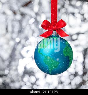 Verschneite Winterkugel weihnachten Ornament hängen mit roter Schleife. Peace on Earth, umweltfreundliches oder winterliches Reisekonzept. Stockfoto