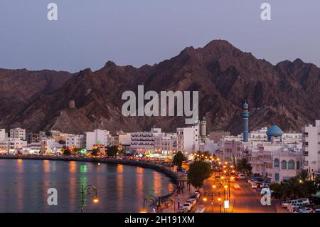 Ein Blick aus dem hohen Winkel auf die Mutrah corniche in der Abenddämmerung: Berge in der Ferne, der Persische Golf darunter. Muttrah, Old Muscat, Muscat, Oman. Stockfoto