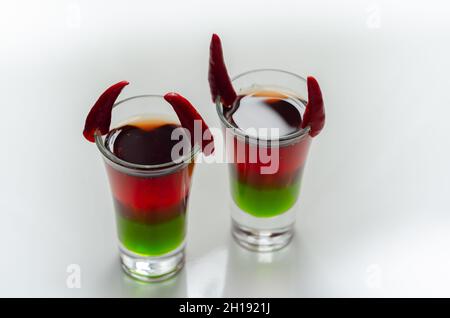 Geschichtetes Getränk, das mit Wodka, grünem Likör, Grenadine und Zitronensaft zubereitet wurde, verziert mit Vogelaugen-Chilis in Form von Hörnern, Teufel geschossen Stockfoto