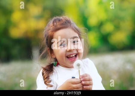 Das hübsche kleine Mädchen lächelt im Park mit der Deladerblüte. Happy niedlichen Kind Spaß im Freien bei Sonnenuntergang. Stockfoto