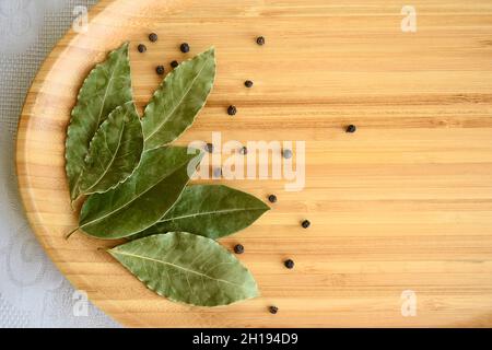 Getrocknete Lorbeerblätter mit schwarzen Pfefferkörnern auf Bambushintergrund, Nahaufnahme. Draufsicht. Speicherplatz kopieren. Selektiver Fokus. Stockfoto