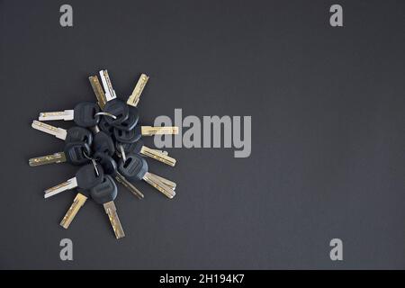 Viele glänzende Metallschlüssel für die Tür, die mit dem Ring auf schwarzem Hintergrund mit leerem Platz für Text oder Notizen zusammengehalten werden Stockfoto