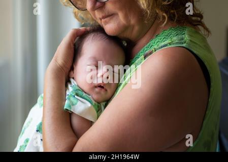 Großmutter hält schlafend 40 Tage alten neugeborenen Jungen am Fenster zu Hause Stockfoto