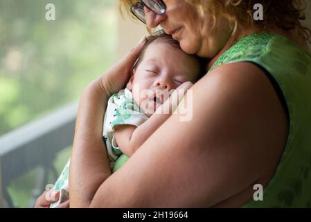 Großmutter hält schlafend 40 Tage alten neugeborenen Jungen am Fenster zu Hause Stockfoto