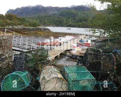 Hummertöpfe und kleine Boote, die an der Anlegestelle in der geschützten Bucht im Dorf Plockton, Wester Ross in den schottischen Highlands, festgemacht sind Stockfoto