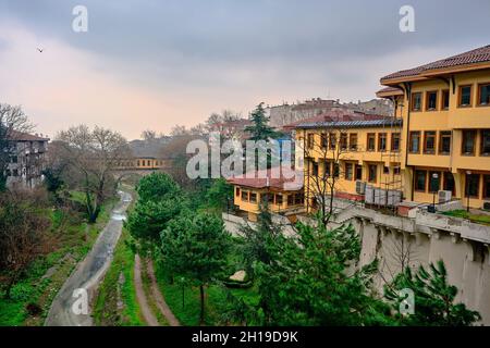 Irgandi-Brücke und Stadtbibliothek in Bursa mit gelber Farbmalerei. Foto aufgenommen am regnerischen Tag und am bewölkten Himmel, einschließlich des Flusses, der vom berg ulu kommt Stockfoto
