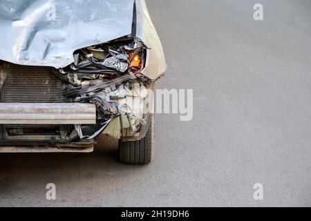 Kaputte Motorhaube des Autos auf der Straße nach Autounfall mit niemand Copyspace. Kaputter Müll im Auto. Kaputter Stoßfänger und Scheinwerfer für das Auto bei schlichtem Licht Stockfoto