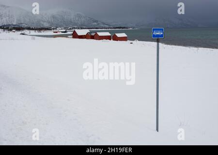 Eine Bushaltestelle und rote Häuser am Meer in einer verschneiten Winterlandschaft. Osvoll, Vesteralen Inseln, Nordland, Norwegen. Stockfoto