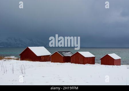 Rote Häuser am Meer in einer verschneiten Winterlandschaft. Osvoll, Vesteralen Inseln, Nordland, Norwegen. Stockfoto