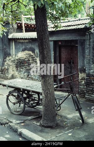 Ein Lastendreirad parkte auf dem Bürgersteig vor einem alten traditionellen Gelände in Peking, China. Stockfoto