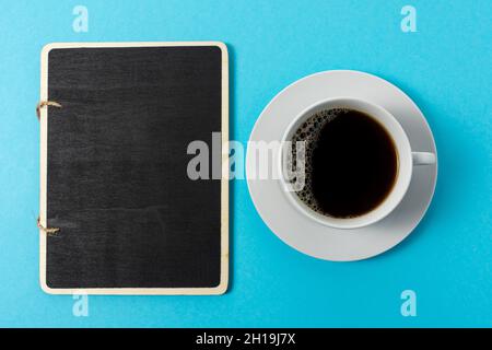 Kreatives Layout mit einer Tasse Kaffee und einem schwarzen Brett auf blauem Hintergrund. Minimales Lebensmittelkonzept. Stockfoto