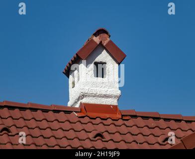 Ein weißer Kamin auf dem Dach aus roten Fliesen Stockfoto