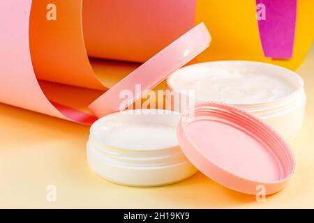 Weißer Kunststoff-Kosmetikbehälter für feuchtigkeitsspendende Creme als Nachbildung auf hellem rosa, orangen und gelben Hintergrund. Körper- und Hautpflege, Gesundheit, Wellnes Stockfoto