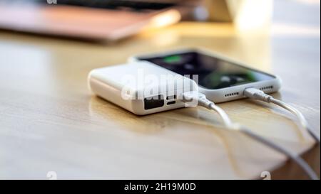 Ein Smartphone wird von einer kleinen weißen Powerbank geladen. Stockfoto
