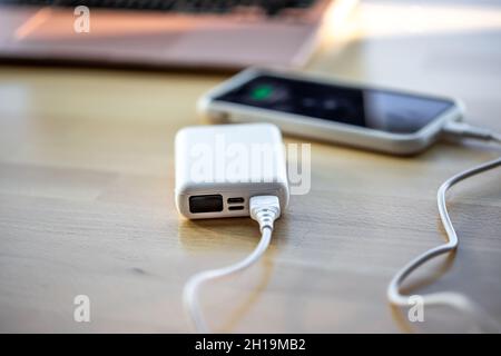 Ein Smartphone wird von einer kleinen weißen Powerbank geladen. Stockfoto