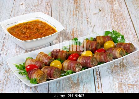 Fleischbällchen in Speckverpackung mit Tomaten und kühlem Souce auf weißem Teller Stockfoto