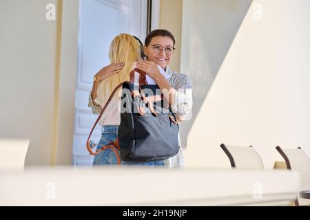 Mama umarmte ihre Tochter im Teenageralter auf der Veranda des Hauses nahe der Eingangstür und trifft Auf Wiedersehen. Stockfoto